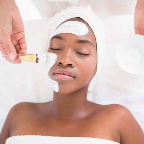 A person receiving a facial treatment, with a cream applied to their face and a towel wrapped around their head.