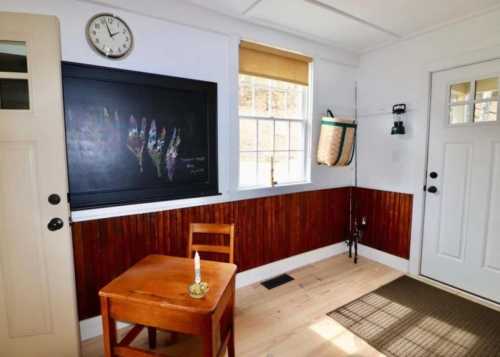 Cozy room with a wooden table, chalkboard, clock, and two doors, featuring warm wood accents and natural light.