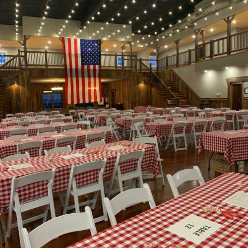 A spacious hall with checkered tablecloths, white chairs, and an American flag hanging from the ceiling.