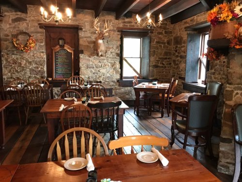 Cozy restaurant interior with wooden tables, chairs, stone walls, and autumn decorations. Warm, inviting atmosphere.