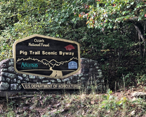 Sign for the Pig Trail Scenic Byway in Ozark National Forest, Arkansas, with lush greenery in the background.