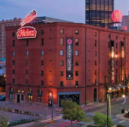 Historic brick building with a large Heinz sign, featuring banners for the History Center, set in an urban landscape.