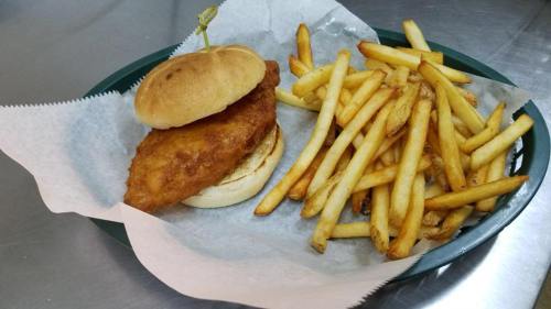 A crispy fried chicken sandwich on a bun, served with a side of golden French fries on a green plate.