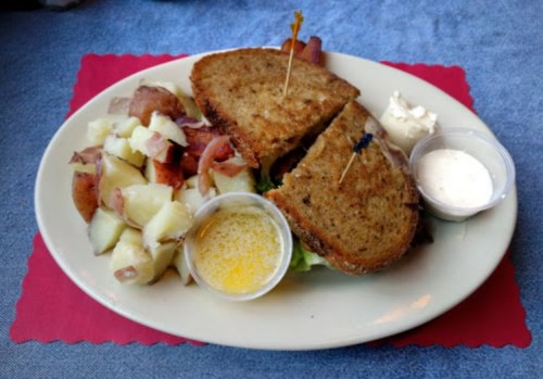 A plate with a sandwich, potato salad, and dipping sauce on a blue tablecloth.