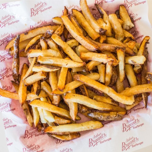 A pile of golden, crispy French fries on a branded paper liner.