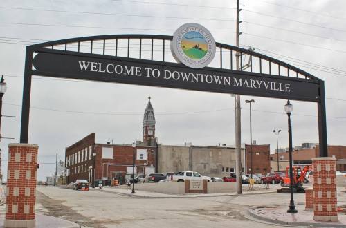 Welcome sign arching over a street in downtown Maryville, with buildings and a clock tower in the background.