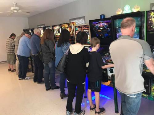 A group of people playing pinball machines in a bright arcade setting.