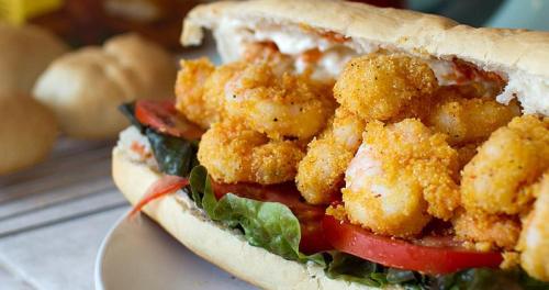 A close-up of a shrimp sandwich with crispy shrimp, lettuce, and tomato in a toasted sub roll.