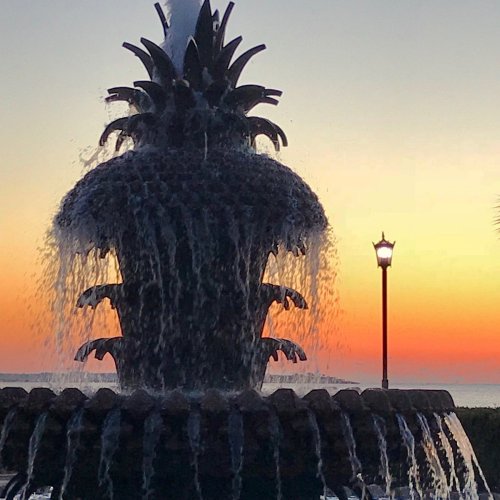 A decorative fountain with flowing water against a vibrant sunset and a lamppost in the background.