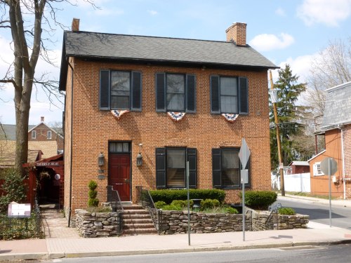 A two-story brick house with black shutters, decorative bunting, and a stone wall, set in a suburban area.