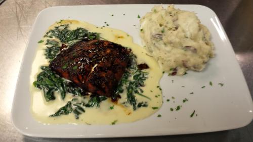 Grilled salmon on a bed of sautéed greens, drizzled with cream sauce, served with creamy mashed potatoes.