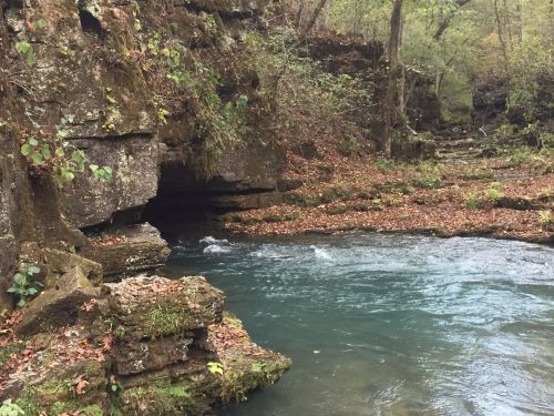 A serene river flows through a rocky landscape, surrounded by trees and autumn leaves.