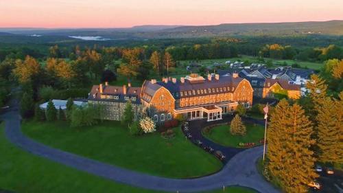 Aerial view of a large, historic hotel surrounded by lush greenery and rolling hills at sunset.