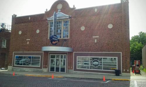 Historic brick building with large windows and a marquee, featuring a circular logo above the entrance.