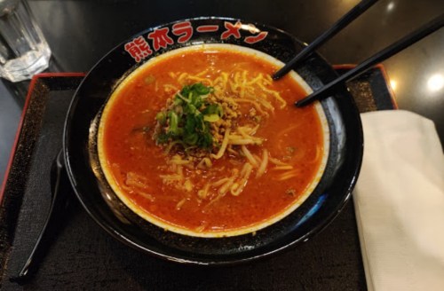 A bowl of spicy ramen topped with green onions and bean sprouts, served with chopsticks on a black tray.