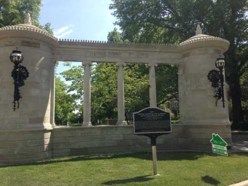 A stone monument with columns and decorative lanterns, surrounded by greenery and a historical marker nearby.