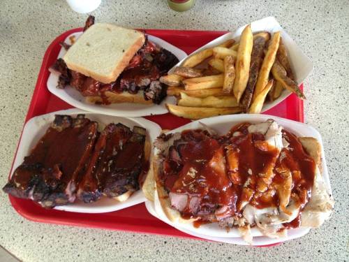A red tray with two sandwiches, ribs, and a side of fries, all topped with barbecue sauce.