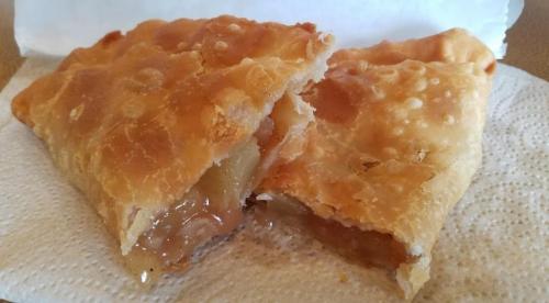 A golden-brown pastry filled with apple filling, partially cut open and resting on a paper towel.