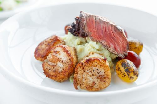 A plate featuring grilled shrimp, sliced beef, and colorful roasted potatoes on a bed of creamy mashed potatoes.