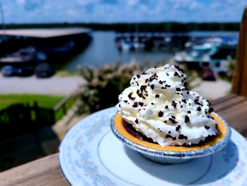 A close-up of a dessert topped with whipped cream and chocolate sprinkles, with a marina in the background.
