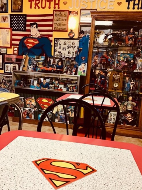 A colorful diner interior featuring Superman memorabilia, including posters, action figures, and themed tables.