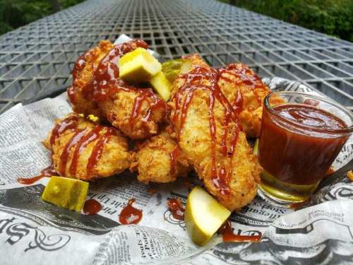A plate of crispy fried chicken wings drizzled with sauce, served with pickles and a small cup of dipping sauce.