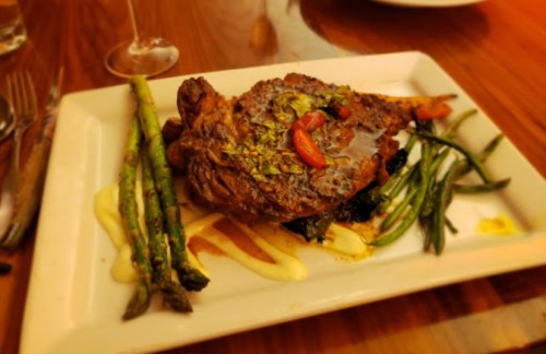 A beautifully plated dish featuring a grilled steak, asparagus, and green beans on a white rectangular plate.