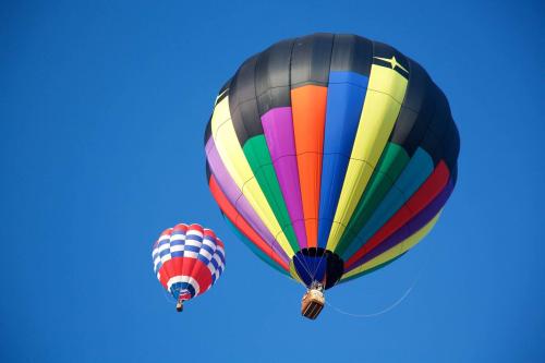 Two colorful hot air balloons float against a clear blue sky, one with stripes and the other in a checkered pattern.