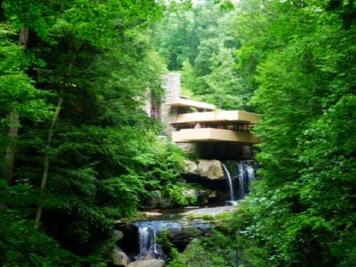 A modern house nestled in lush green trees, with a waterfall cascading nearby, blending harmoniously with nature.