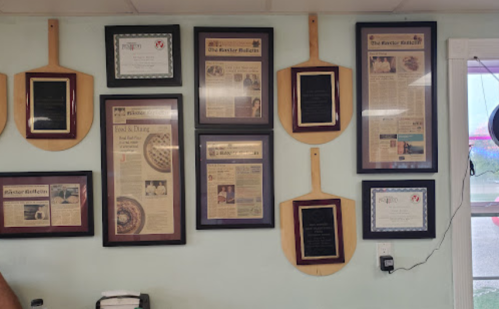 A wall display featuring framed articles and awards, alongside wooden pizza peels, in a casual dining setting.