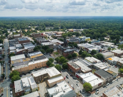 Aerial view of a small town with buildings, trees, and a cloudy sky in the background.