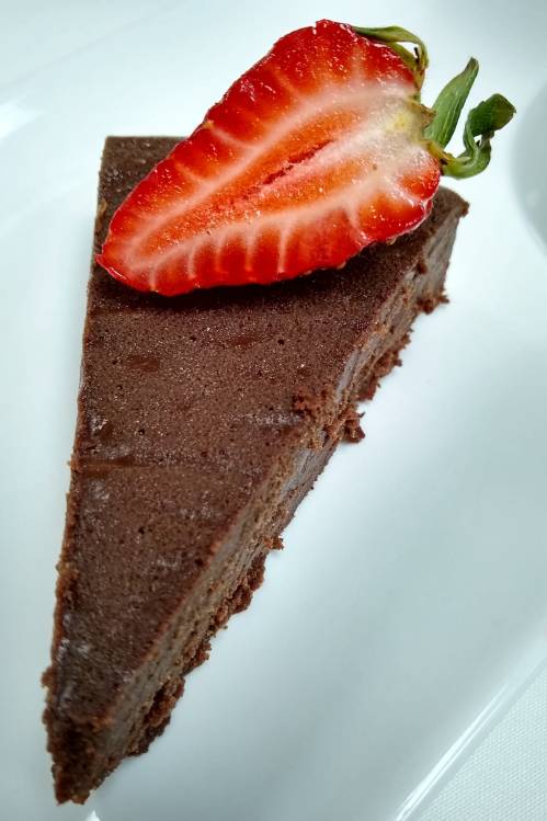 A slice of rich chocolate cake topped with a fresh strawberry on a white plate.