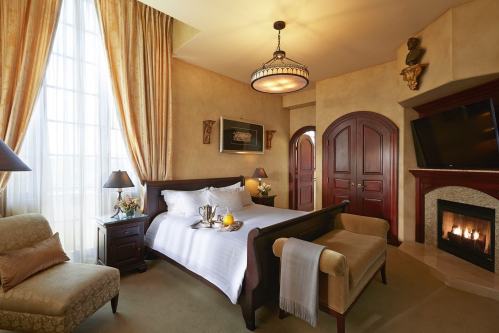 Cozy hotel room with a king bed, elegant decor, a fireplace, and large windows letting in natural light.