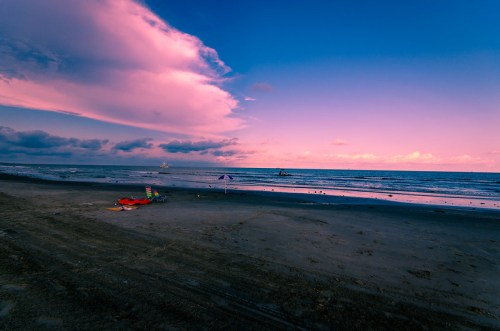 A serene beach at sunset, with colorful chairs and gentle waves under a vibrant sky filled with clouds.