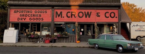 A vintage storefront with "M. Crow & Co." sign, featuring groceries and sporting goods, alongside a classic green car.