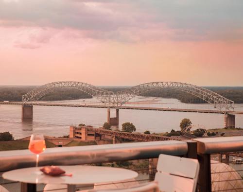 A scenic view of a bridge over a river at sunset, with a cocktail glass on a table in the foreground.