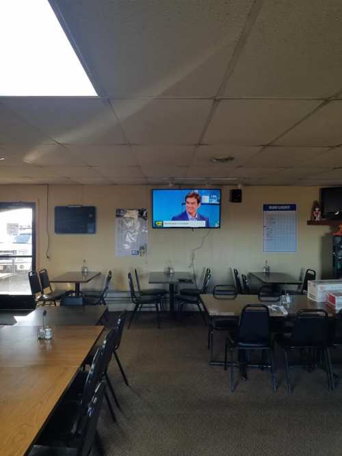 A restaurant interior with empty tables and chairs, featuring a TV displaying a news program on the wall.