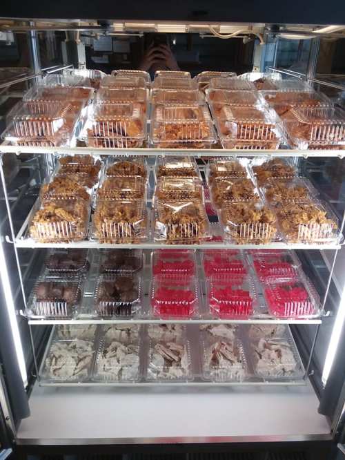 A display case filled with various desserts in clear containers, including brownies, bars, and colorful treats.
