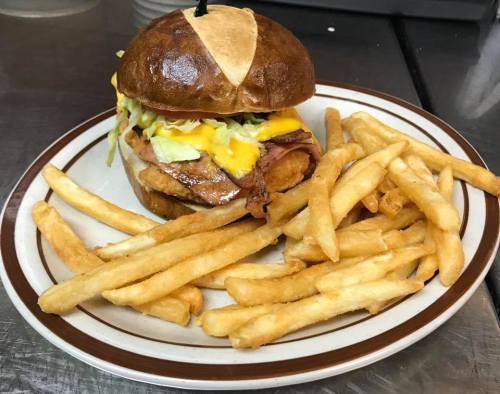 A delicious burger with cheese, lettuce, and ham, served with a side of golden French fries on a plate.