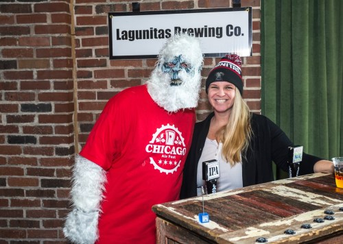 A person in a yeti costume poses with a woman at a brewery, both smiling in front of a bar with beer glasses.
