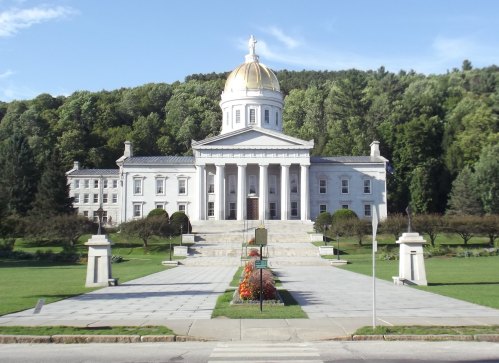 A grand building with a golden dome, surrounded by greenery and landscaped gardens, set against a clear blue sky.