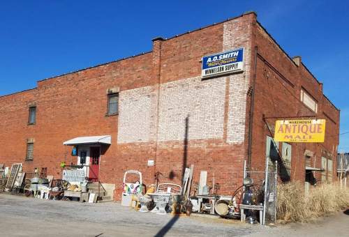 A brick building with a sign for an antique mall, surrounded by various items for sale outside.