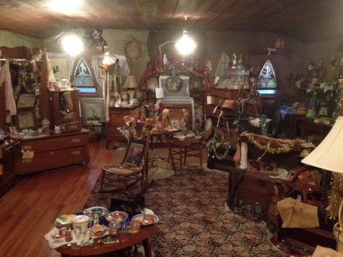 A cluttered room filled with vintage furniture, decorations, and various collectibles, illuminated by overhead lights.