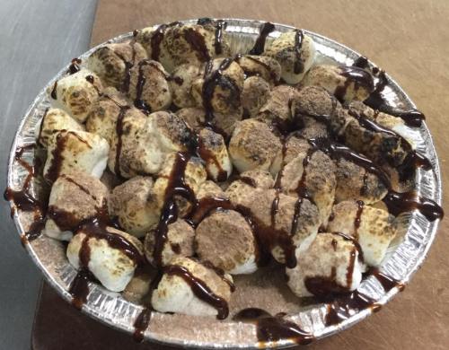 A pie dish filled with toasted marshmallows drizzled with chocolate and sprinkled with cocoa powder.