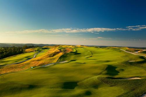 A scenic view of a lush green golf course under a clear blue sky, with rolling hills and a winding path.