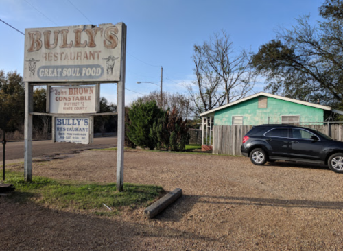 Sign for Bully's Restaurant, advertising "Great Soul Food," with a car parked nearby and a green house in the background.