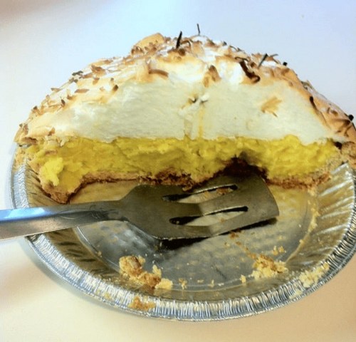 A slice of lemon meringue pie with a golden filling and fluffy meringue topping, served in a pie tin.