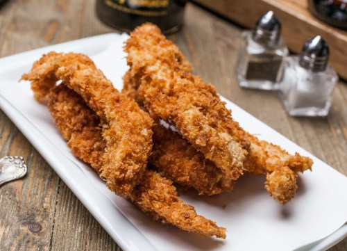 Crispy fried chicken tenders served on a white plate, with salt and pepper shakers in the background.