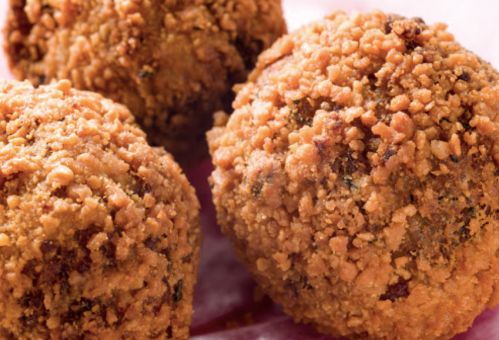 Three golden-brown, crispy fried balls with a crunchy coating, placed on a pink surface.
