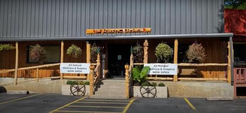 Exterior of a rustic store with wooden features, planters, and signs stating "All Natural Wellness & Supply NOW OPEN."
